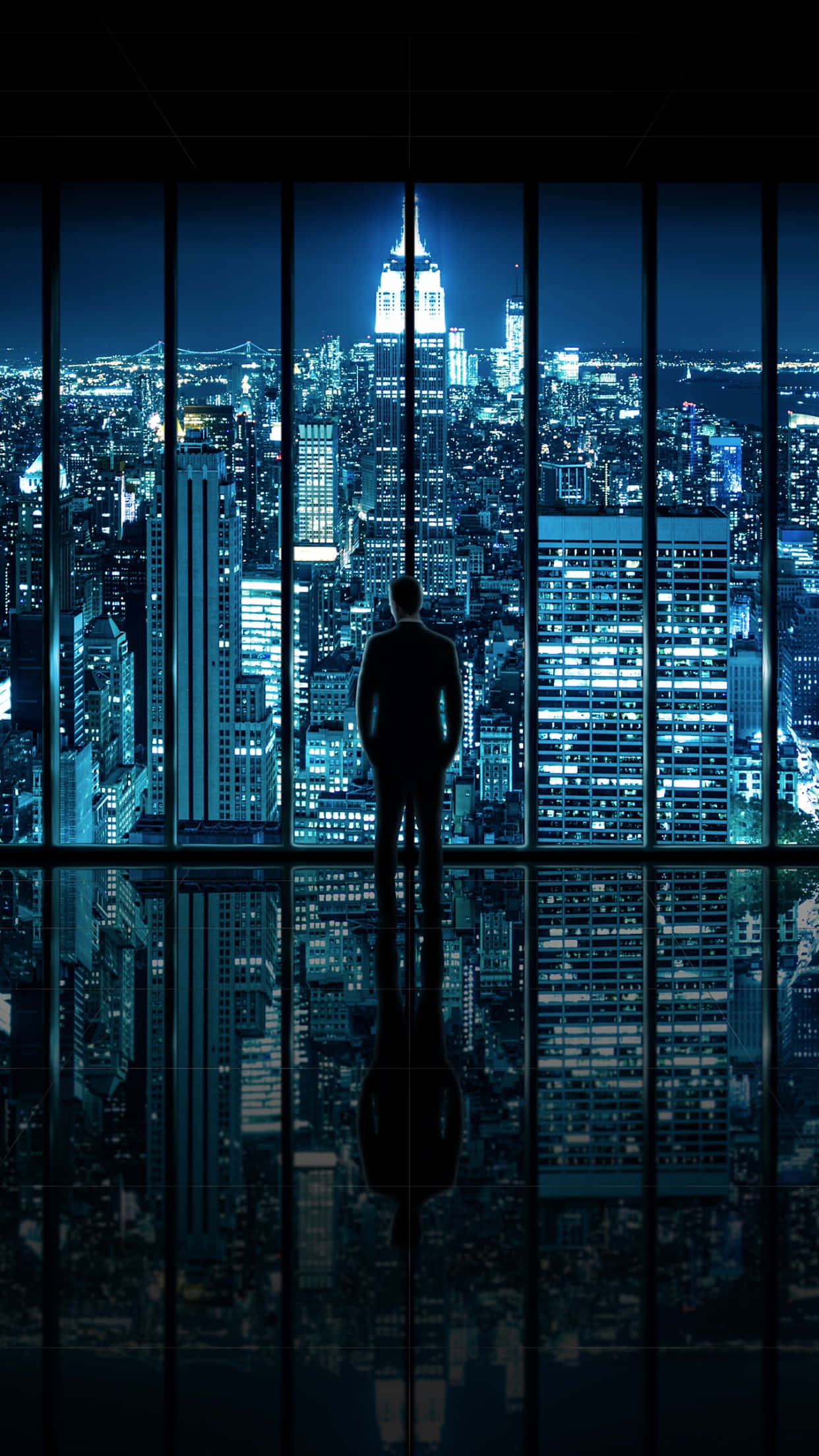 以紐約市的喧囂為靈感，為您的iPhone Xs設置壁紙 壁紙 — 一個孤獨的剪影站在窗前，窗外是夜晚藍色燈光璀璨的城市景觀，下方有清晰的倒影。