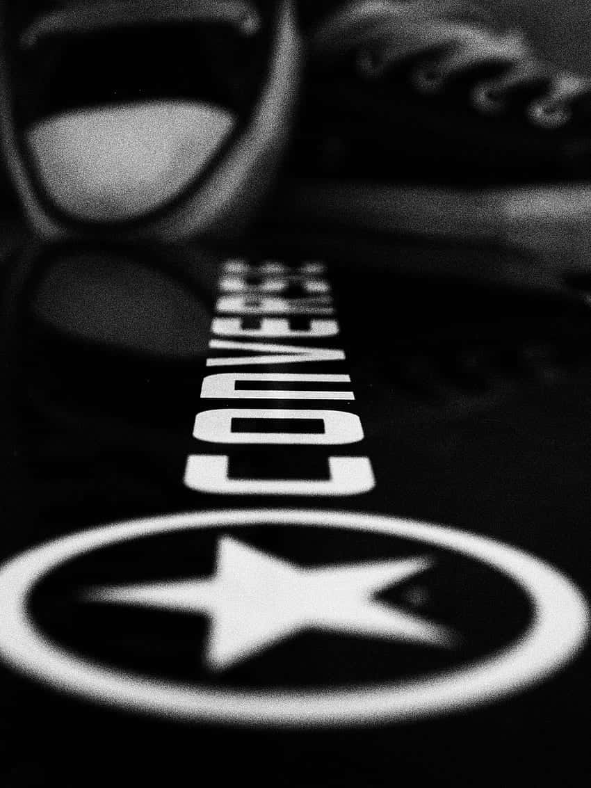 以經典Converse造型展現你的創意與個性 壁紙 — 黑白特寫，Converse 運動鞋標誌投射在反光表面上，背景有模糊的鞋子。