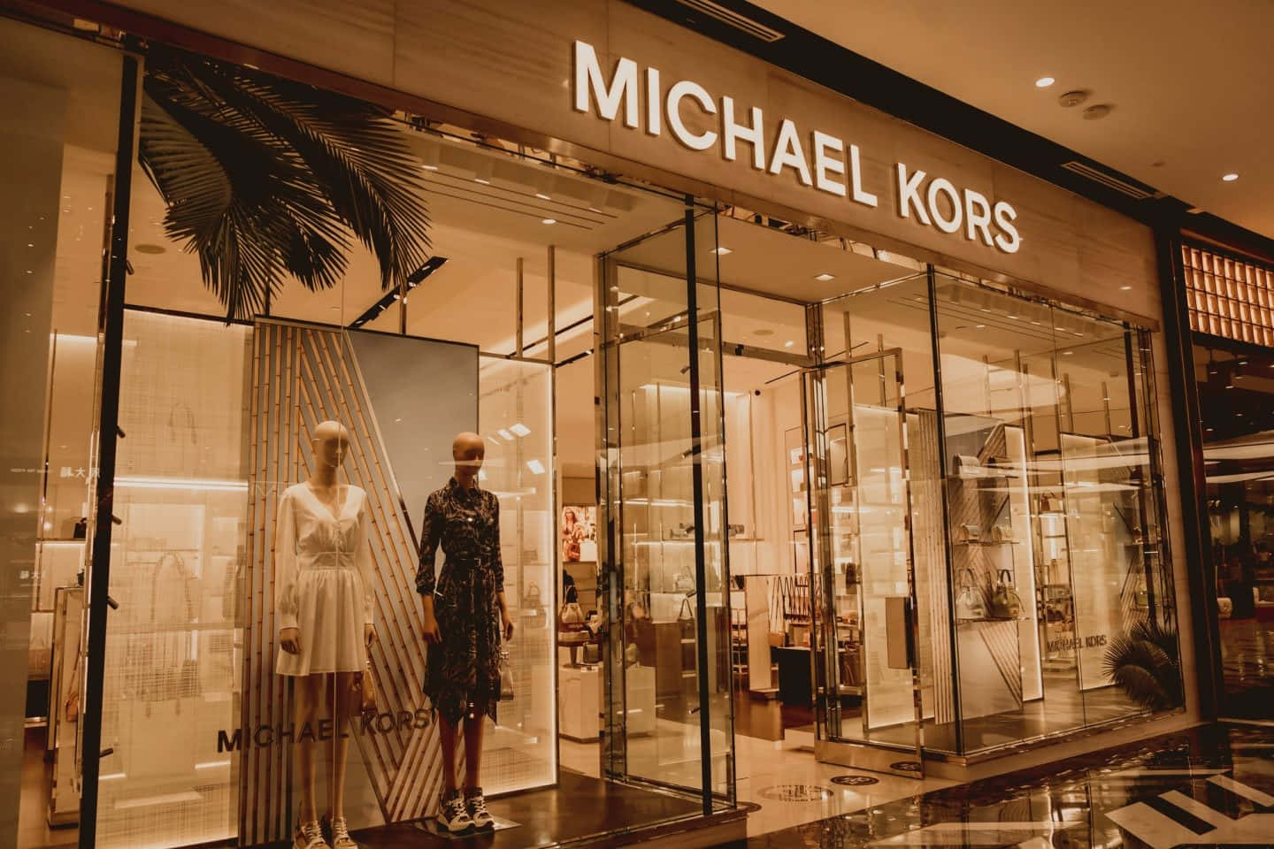夜間Michael Kors時裝店，有人體模型和棕櫚裝飾。