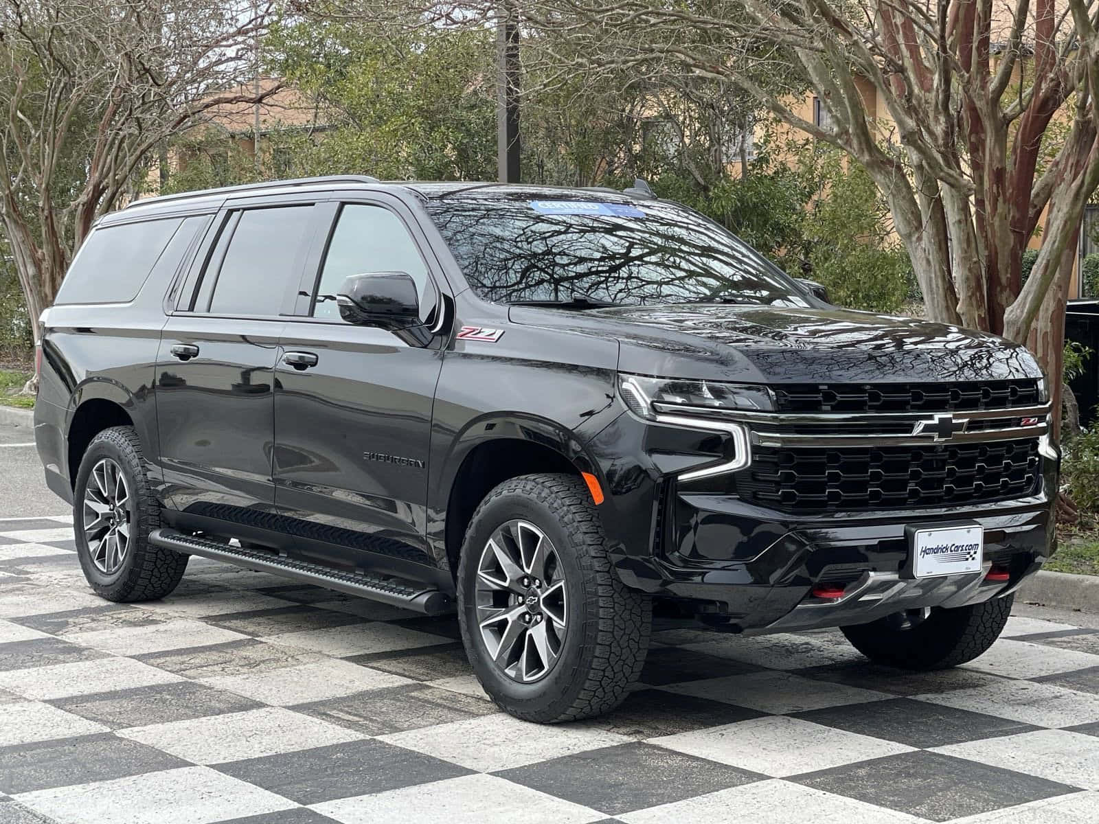 以經典雪佛蘭吸引眾人目光 壁紙 — 一輛時尚的黑色雪佛蘭 Suburban Z71 SUV 停放在棋盤格路面，周圍是落葉樹木。