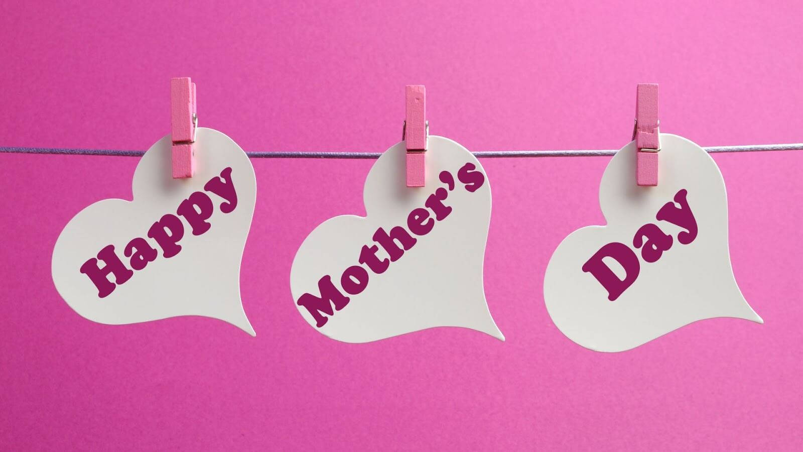 三個心形卡片，上面有「Happy Mother's Day」文字，夾在鐵絲上，背景為粉紅色。
