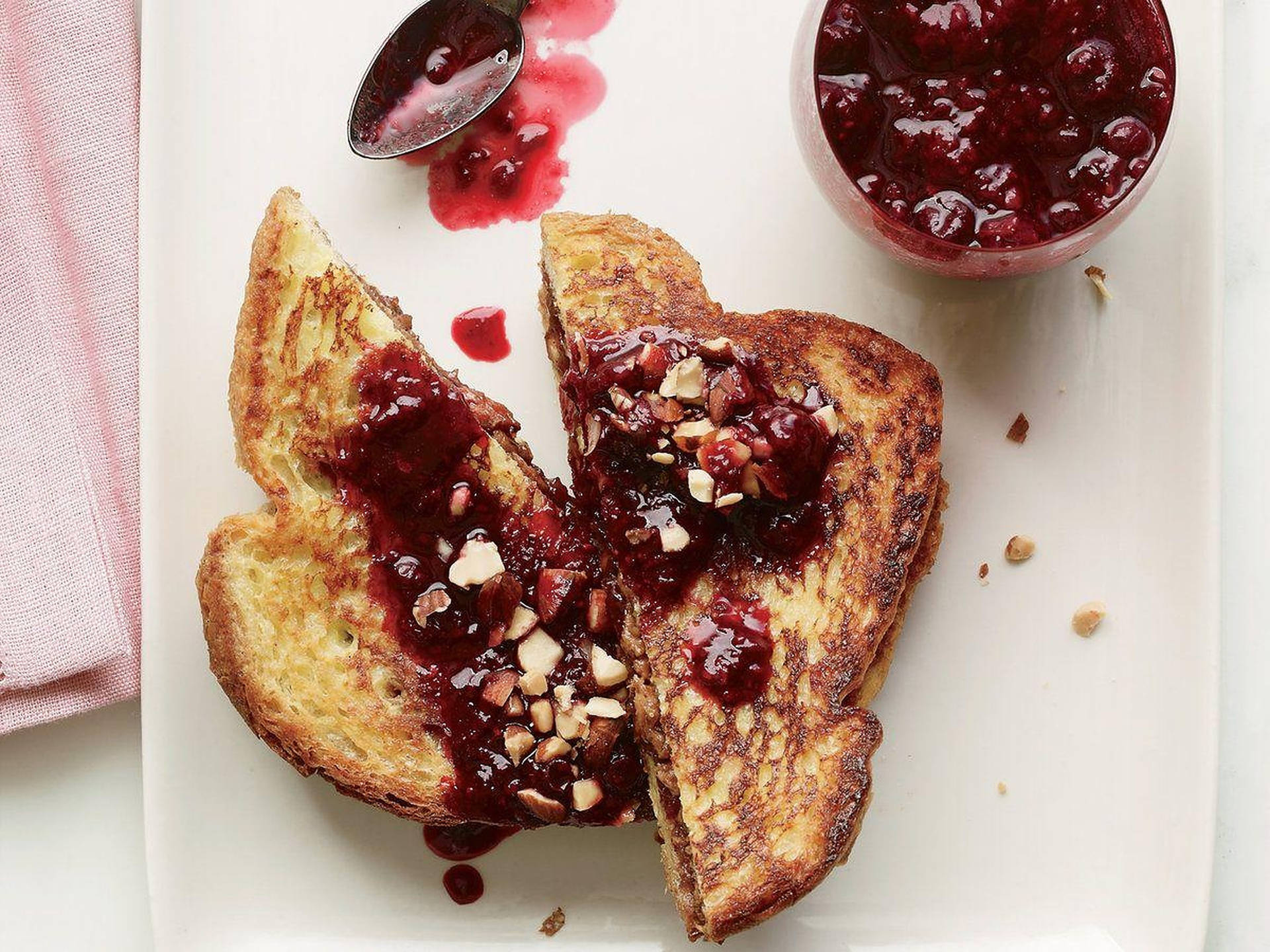 法式吐司配蔓越莓醬和堅果，放在白色碟子上，附有粉紅色餐巾。