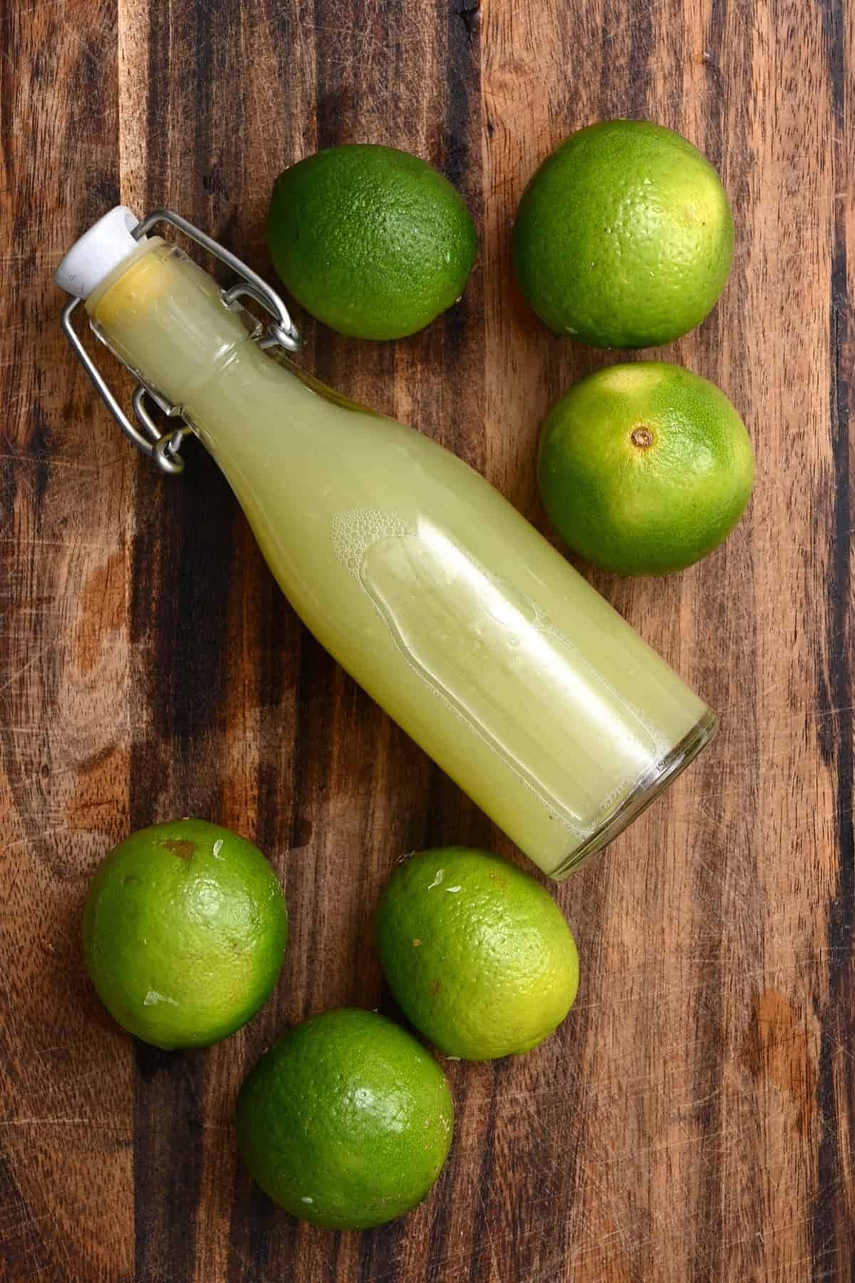以美味青檸為您提神醒腦！ 壁紙 — 一瓶新鮮青檸汁的玻璃瓶放在一塊質樸的木板上，周圍環繞著整個青檸。