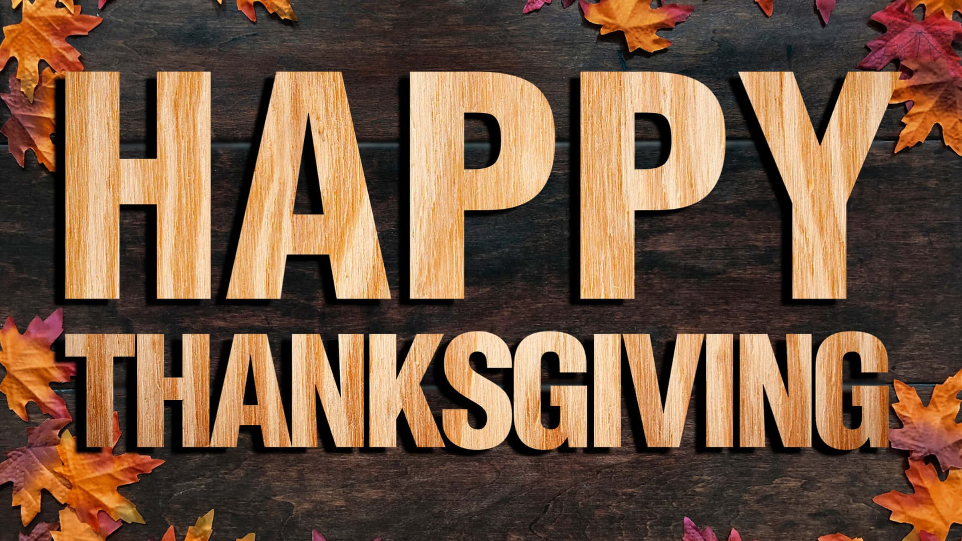 深色木質上帶有秋葉和木製字母的 Happy Thanksgiving 文字。