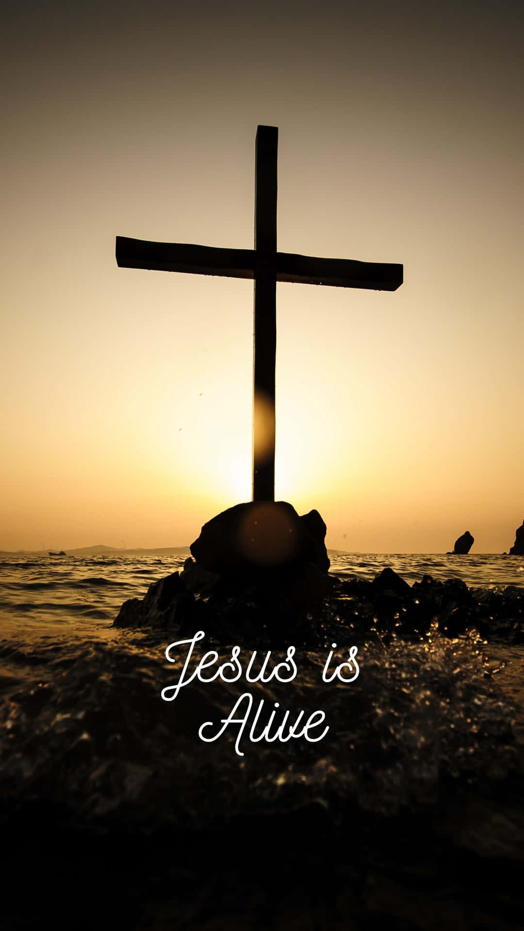 日落時岩石上十字架的剪影，伴隨海浪和文字 Jesus is Alive