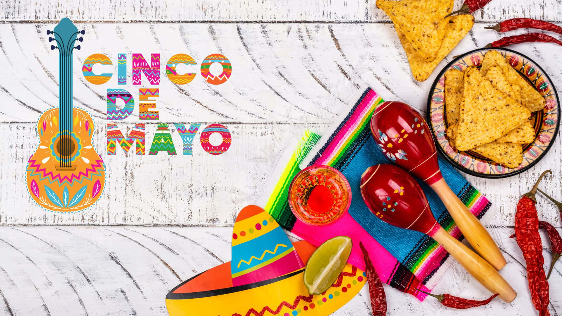 以色彩繽紛的裝飾慶祝五·五節 壁紙 — 充滿活力的 Cinco de Mayo 慶祝物品，如結他、沙槌、闊邊帽和薯片，排列在質樸的白色木質表面上。