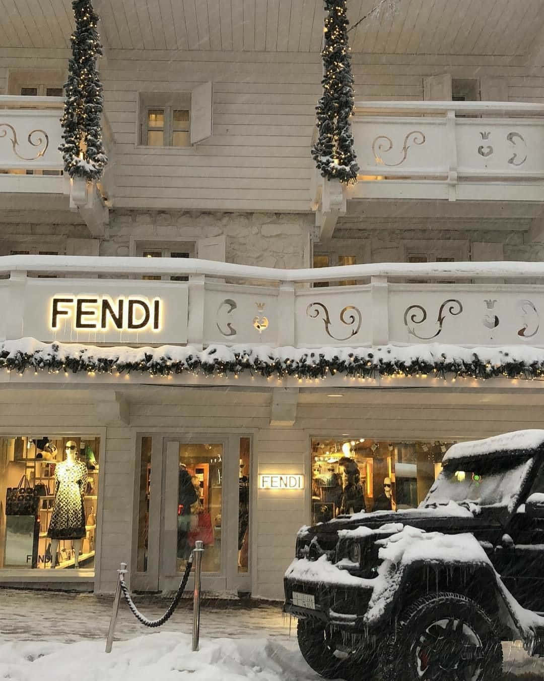 以芬迪時尚男裝提升你的造型 壁紙 — 一間被雪覆蓋的FENDI精品店，帶有節日燈飾，一輛黑色SUV停在外面，冬日天空下。