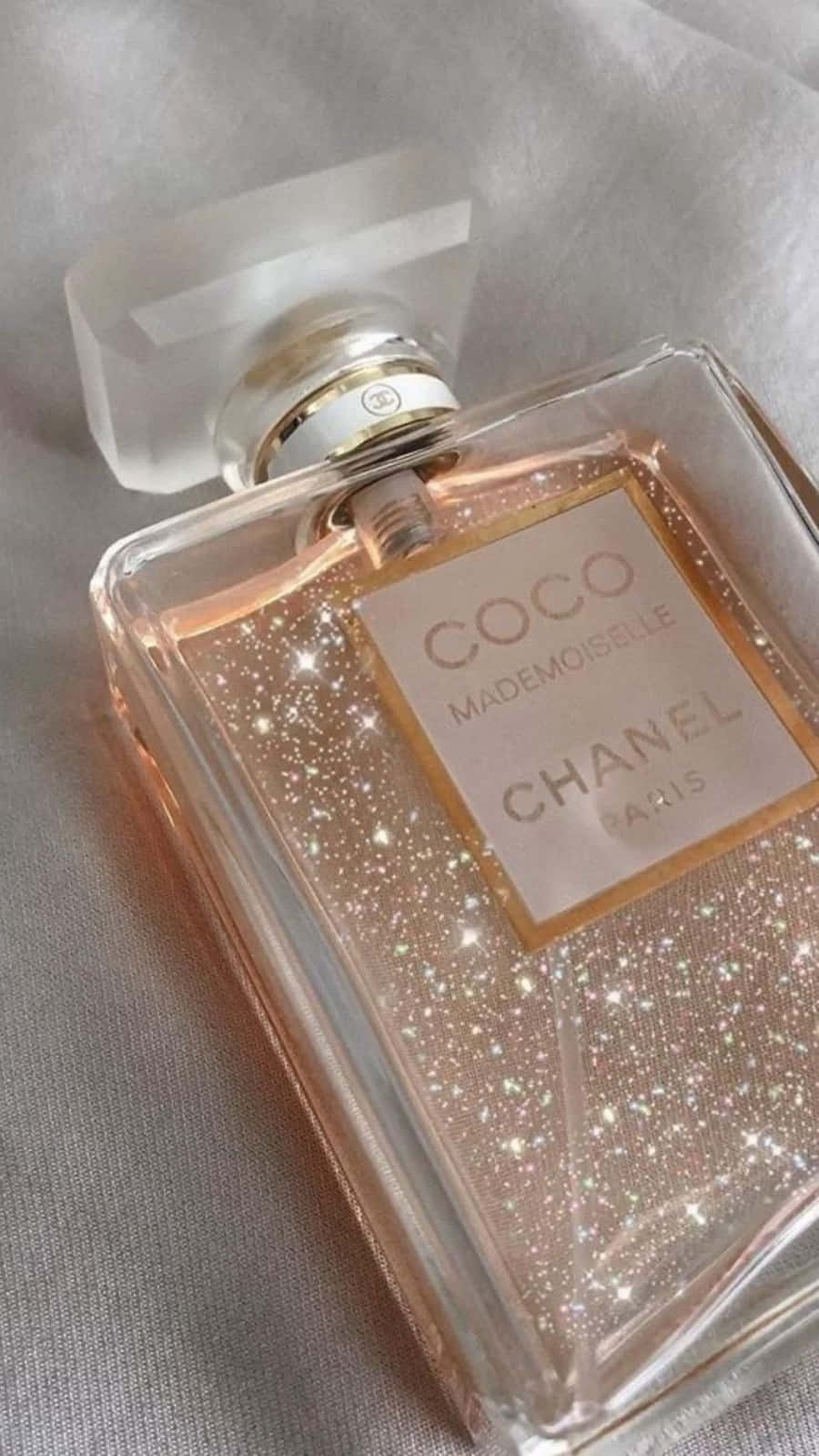 一個玫瑰金色閃閃發光的 Chanel 香水瓶放在柔軟的布料上。