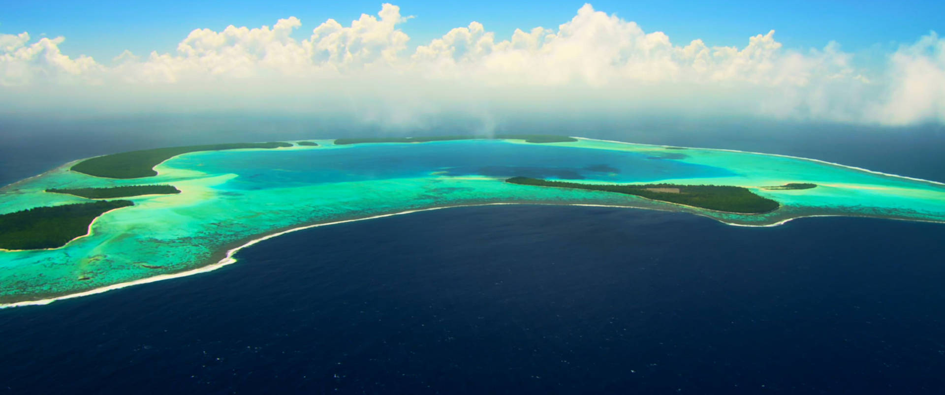 熱帶環礁的空中景觀，有藍綠色潟湖和綠色島嶼。