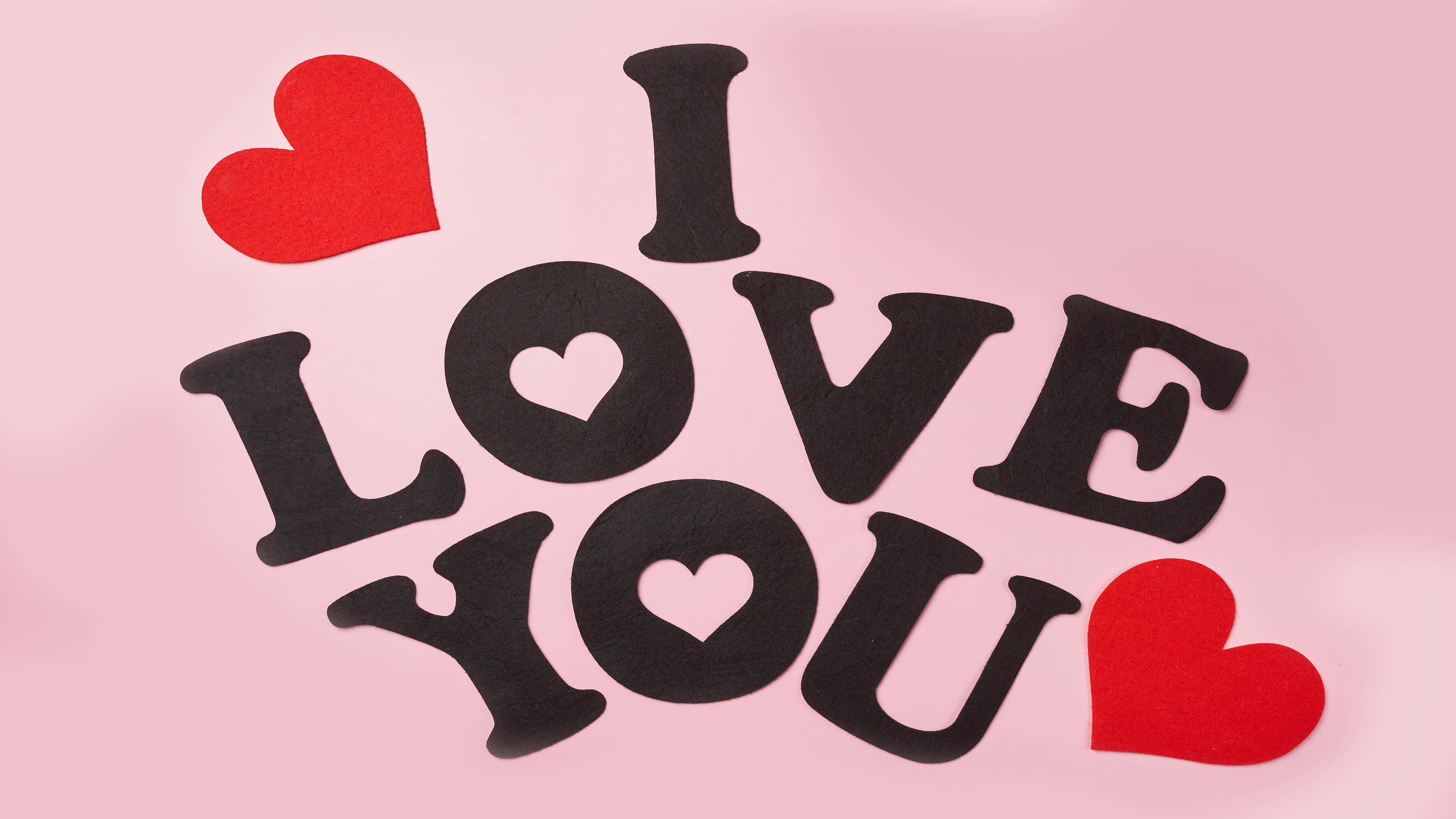 以超高清3840X2160顯示器釋放潛能 壁紙 — 黑色氈字拼出 I LOVE YOU，配上紅色心形，在柔和的粉紅色背景上。