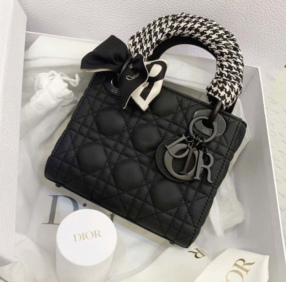 以迪奧藝術詮釋女性之美 壁紙 — 黑色絎縫Dior Lady Dior手袋，配有千鳥格手柄和蝴蝶結，放置在帶有Dior配件的白色盒子中。