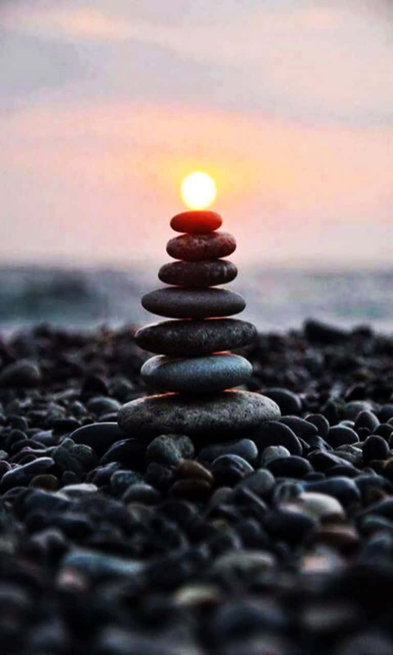 海灘上堆疊的石頭，頂部有發光球體，日落時分 — 禪 壁紙