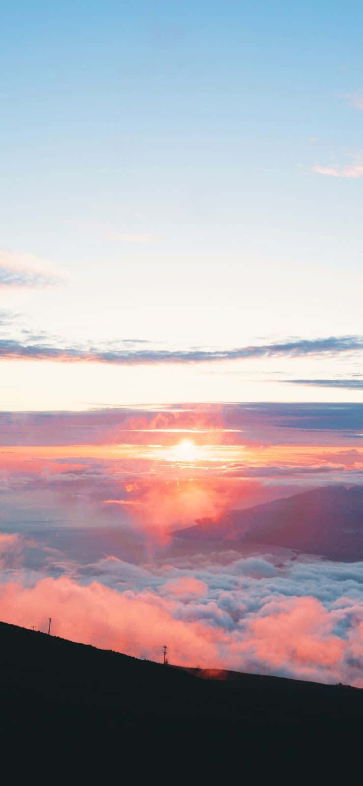 以這款唯美夕陽壁紙，捕捉自然之美 壁紙 — 夕陽將雲彩染成火熱的橙色和粉紅色，同時沉入山脊之下，投下長長的陰影。