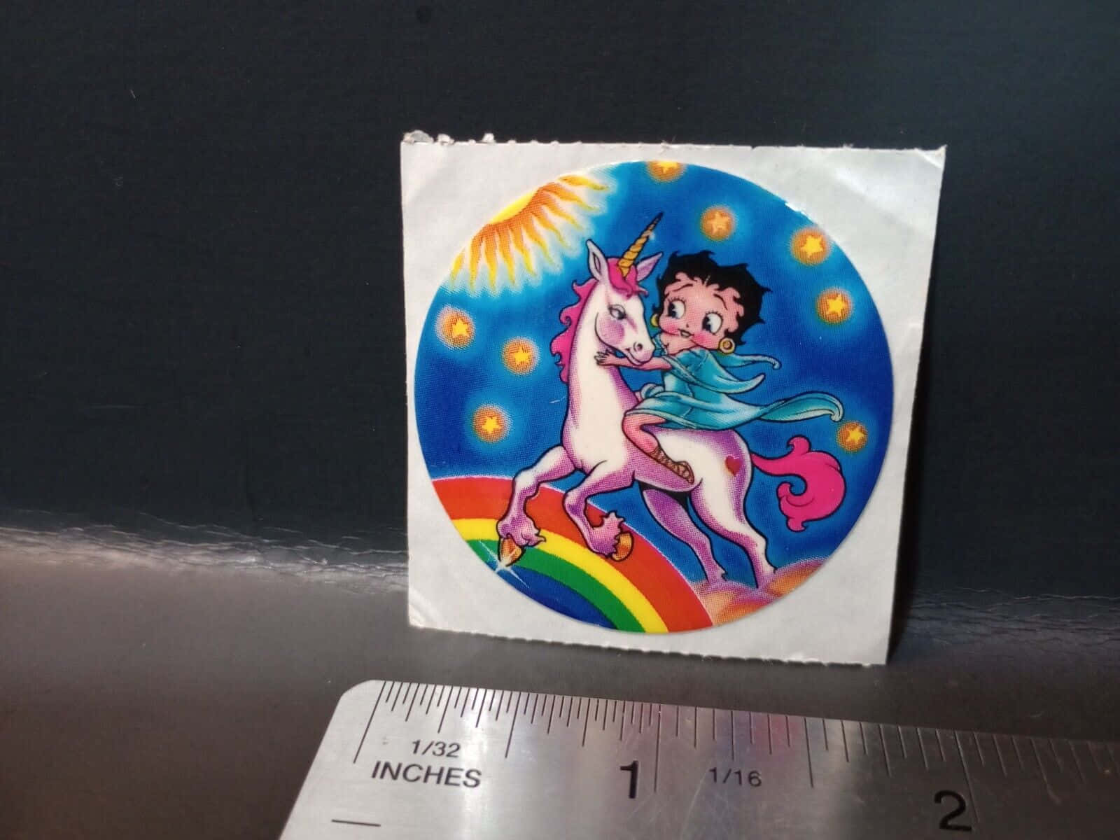 Betty Boop 騎著粉紅色獨角獸在彩虹上，伴有星星和太陽。