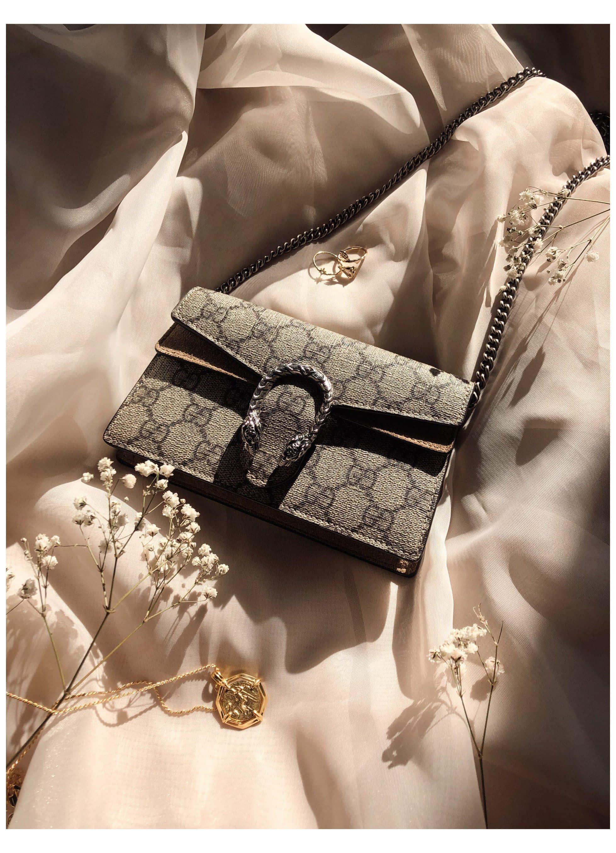 以這款時尚現代手袋更顯奢華 壁紙 — 一個奢華的Gucci Dionysus手袋優雅地放在柔軟的奶油色布料上，旁邊有乾花和金飾，在溫暖的陽光下。