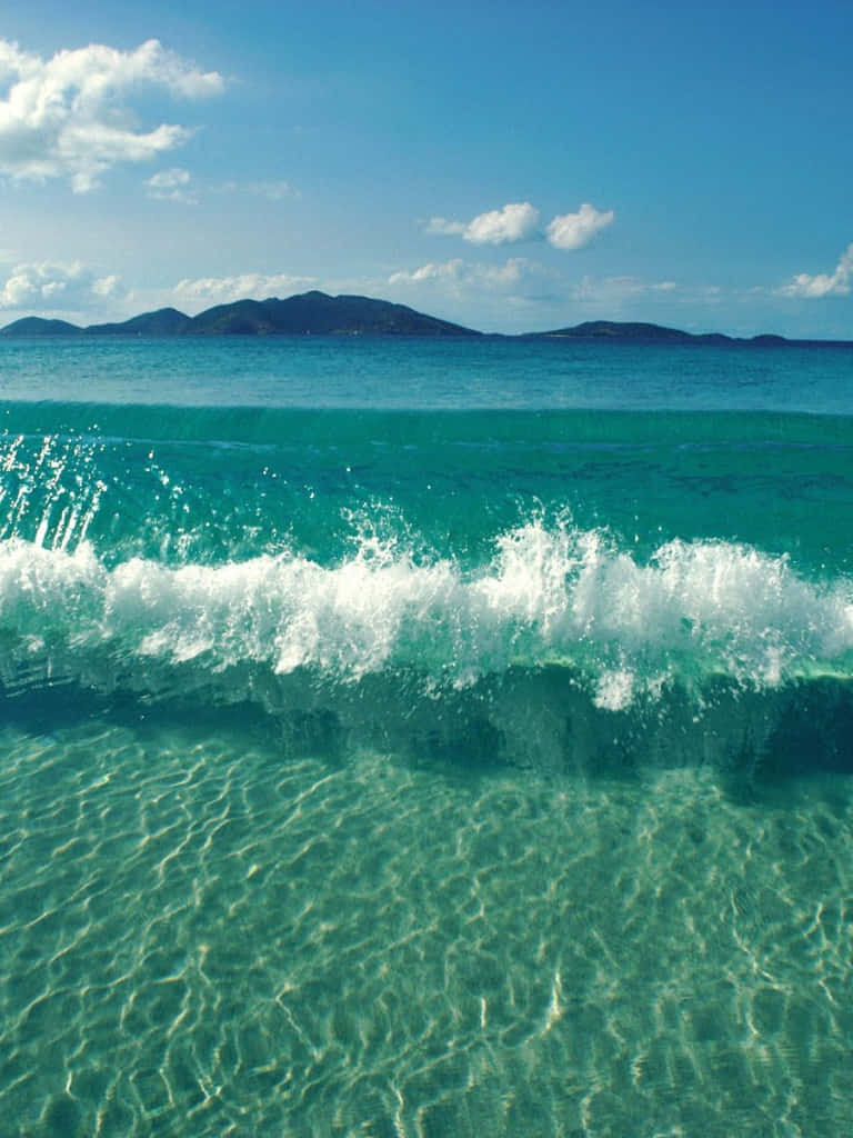 藍綠色海浪拍打沙質海底，遠方島嶼在藍天下。