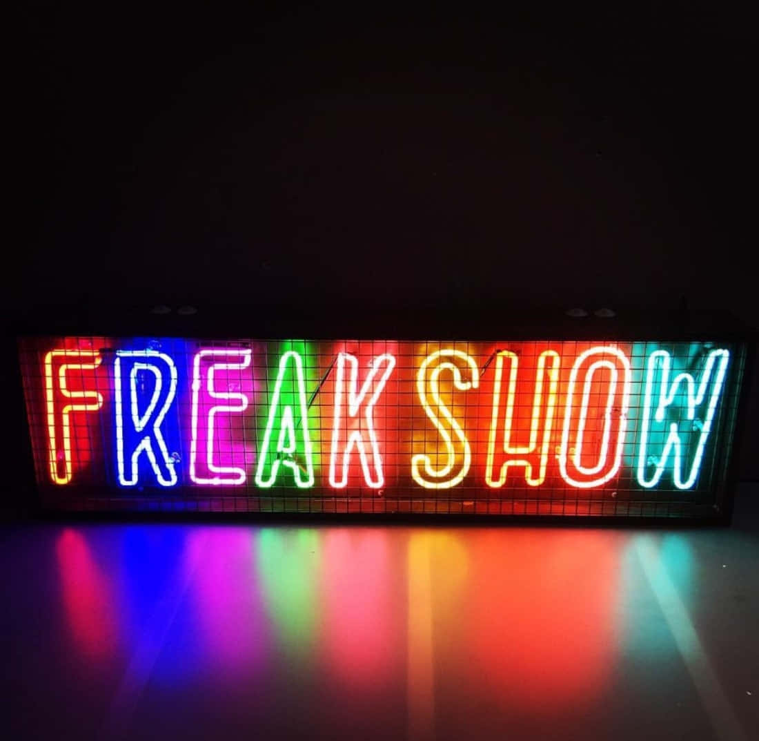 一個色彩繽紛的霓虹燈牌，上面寫著 freak show，彩虹燈光在黑暗表面上反射。
