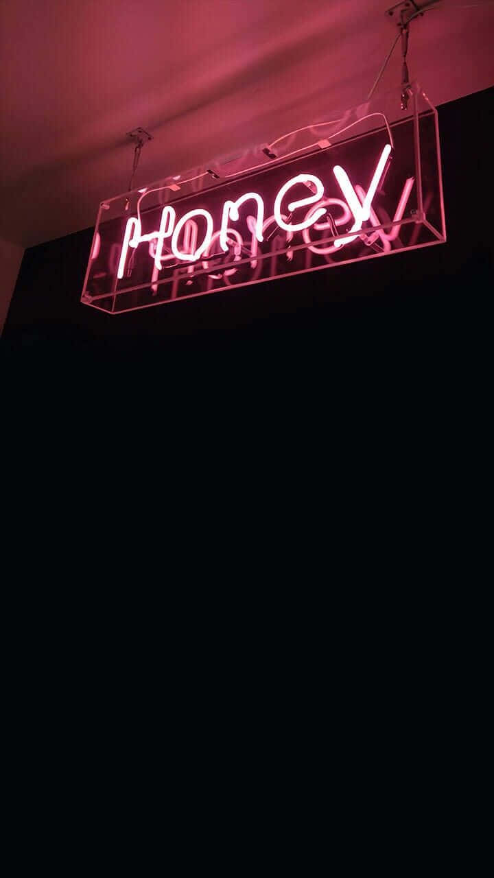 以霓虹燈點亮夜晚 壁紙 — 一個發光的粉紅色霓虹燈牌，上面拼寫著 'HONEY'，懸掛在黑暗的房間中，散發出柔和的光芒。