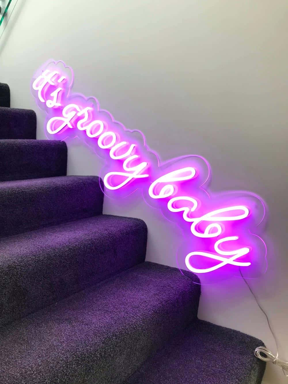 紫色霓虹燈牌，上面寫著「it's groovy baby」，安裝在鋪有地毯的樓梯旁邊的牆上。