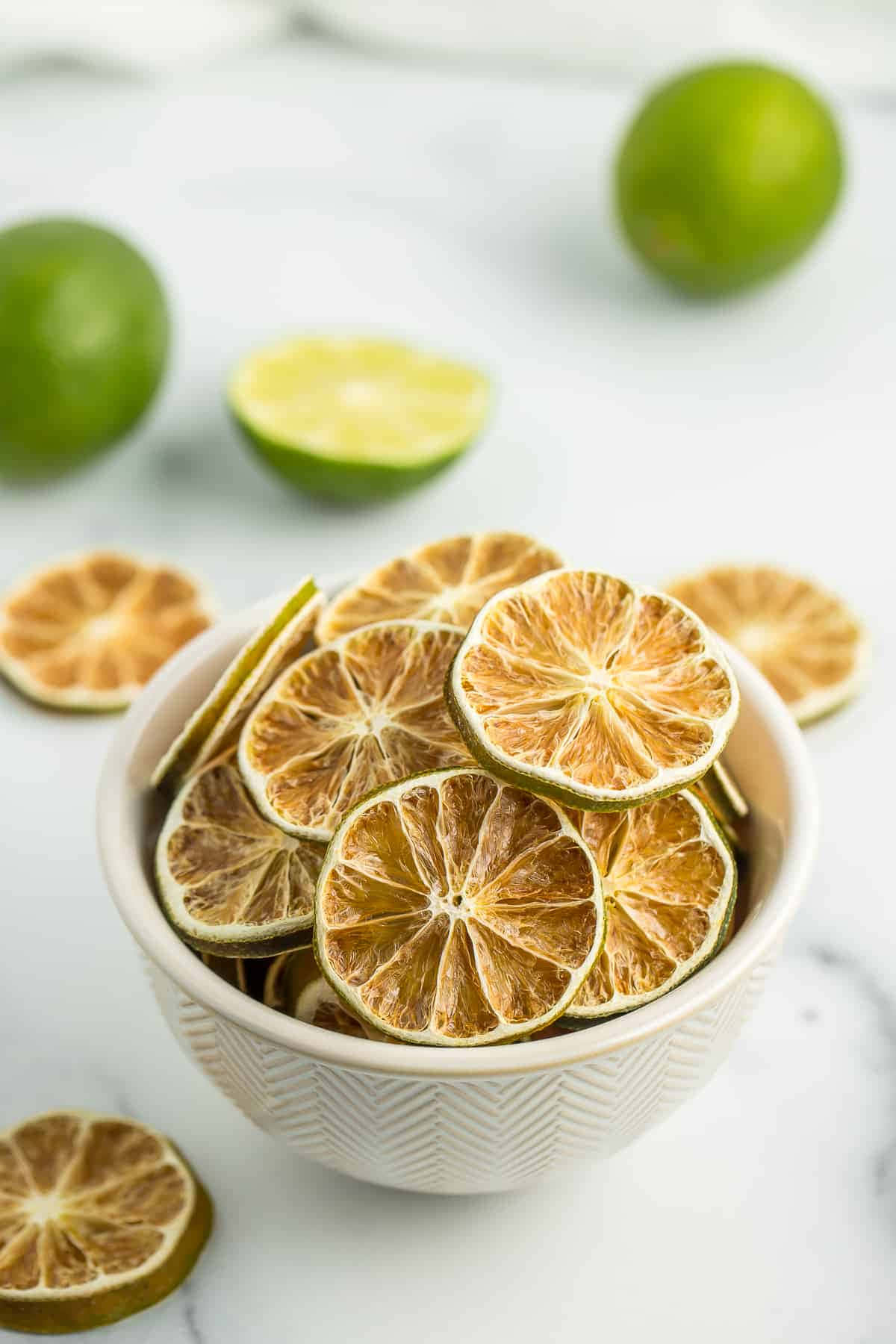 以青檸點亮您的每一天 壁紙 — 一個白色碗裝滿了乾青檸片，放在大理石表面上，周圍是新鮮的綠色青檸。