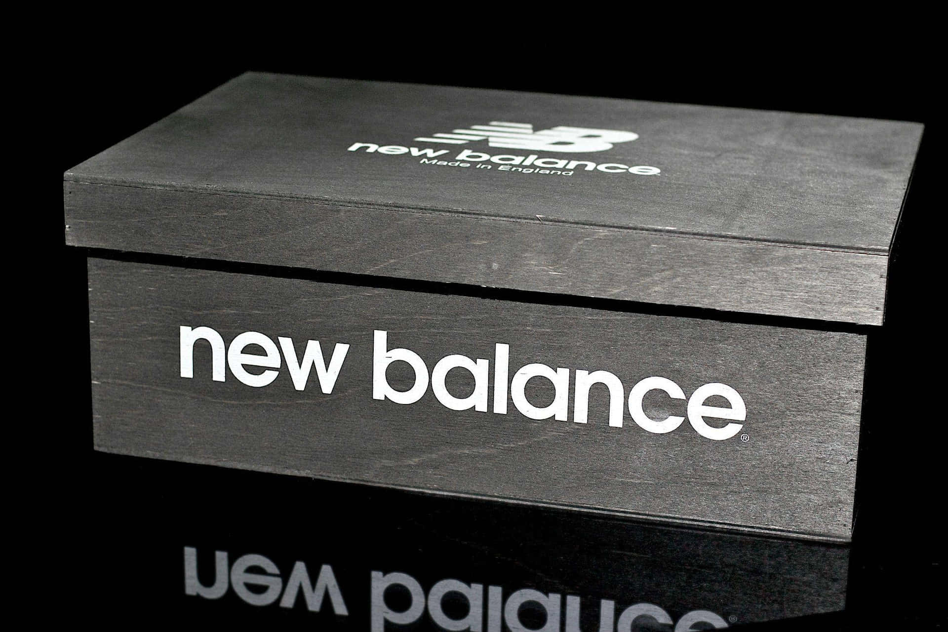 黑色New Balance鞋盒，帶有白色標誌，置於反射表面。