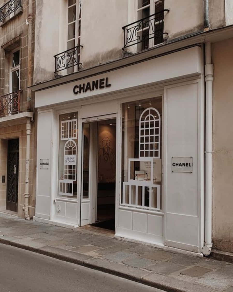 以香奈兒提升日常造型 壁紙 — 一間時尚的白色Chanel精品店，擁有拱形窗戶和華麗的陽台，排列在一條安靜的歐洲鵝卵石街道上。