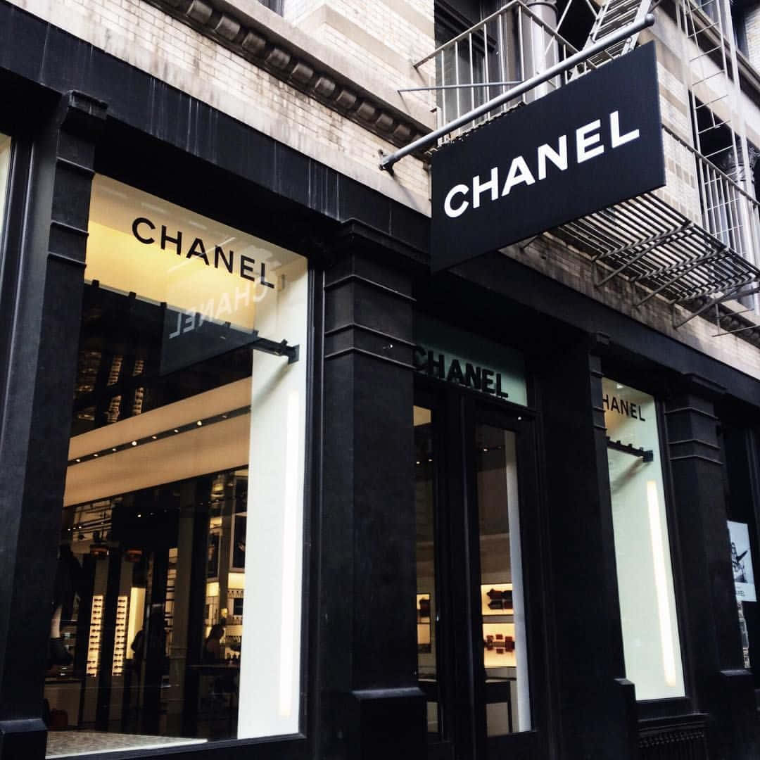 「以香奈兒活出生活」 壁紙 — 一間時尚的黑色 Chanel 精品店，櫥窗亮著燈，在雨中的城市背景下展示奢侈品。