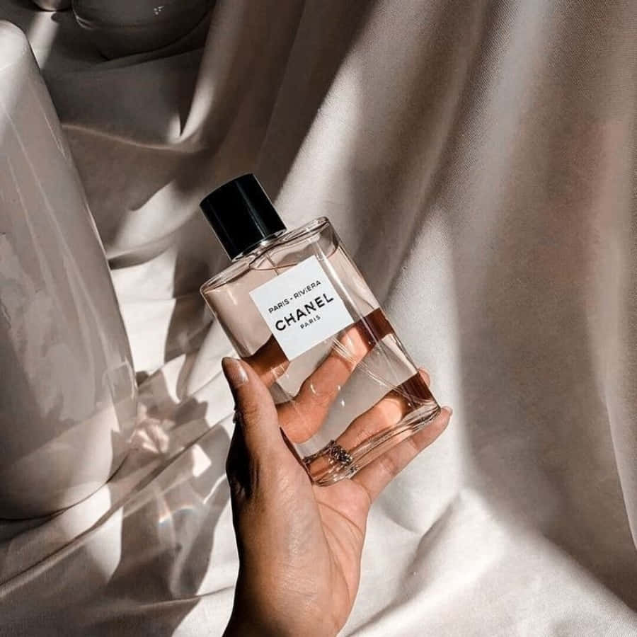 手拿著Chanel Paris Riviera香水瓶，放在帶有陽光的米色布料上。