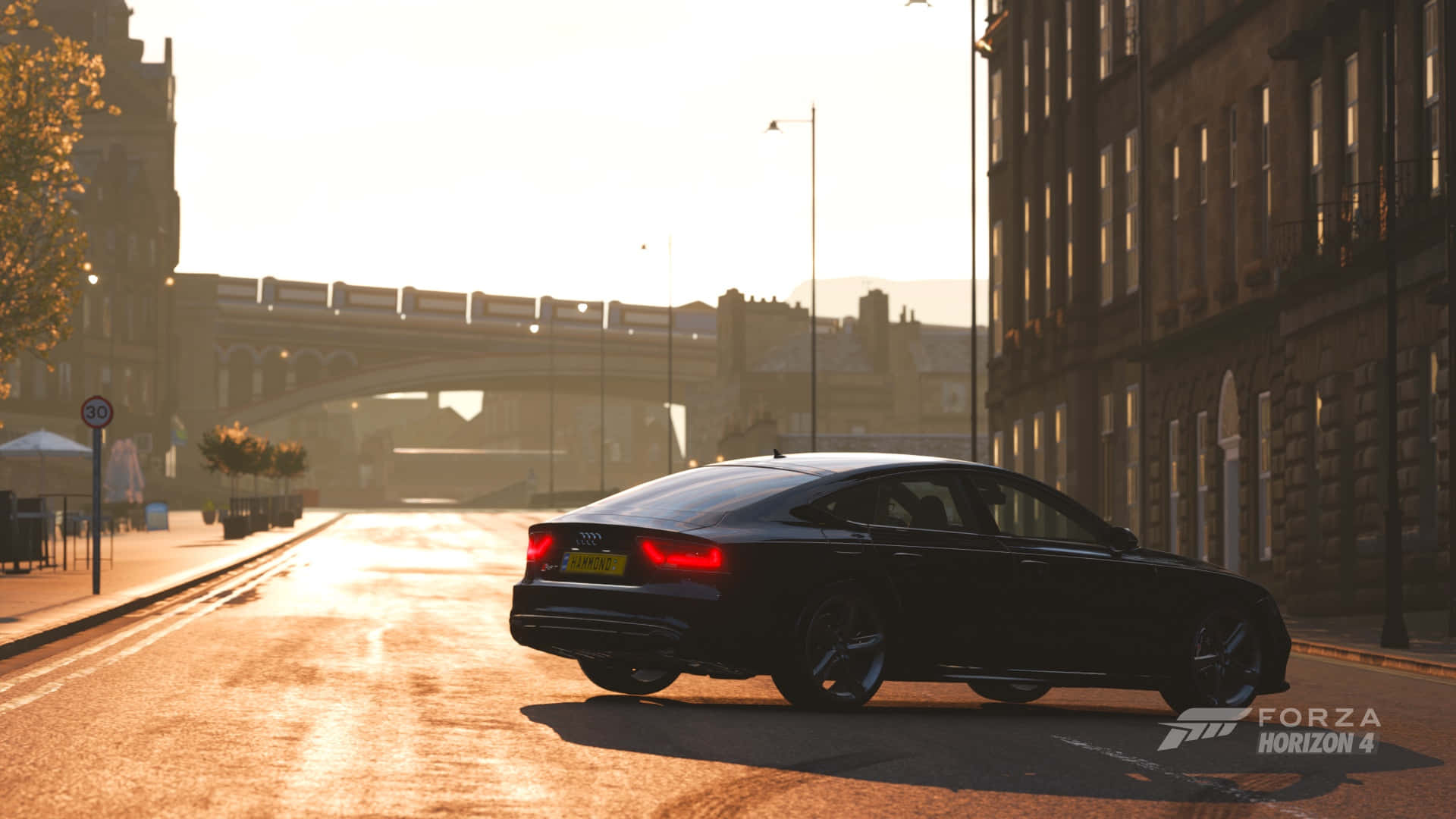 以高清畫質體驗高燃賽車遊戲《Forza Horizon 4》 壁紙 — 一輛時尚的黑色奧迪轎車在陽光明媚的黃金時段沿著城市街道滑行，溫暖的光線反射在潮濕的路面和歷史建築上。