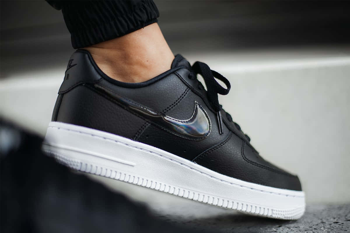 黑色Nike Air Force 1運動鞋，帶全息Swoosh標誌，置於混凝土階梯上。