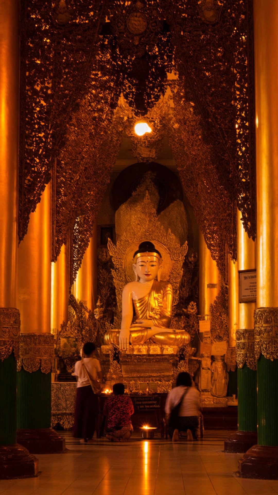 人們在溫暖燈光的寺廟中，在金色佛像前跪拜祈禱。