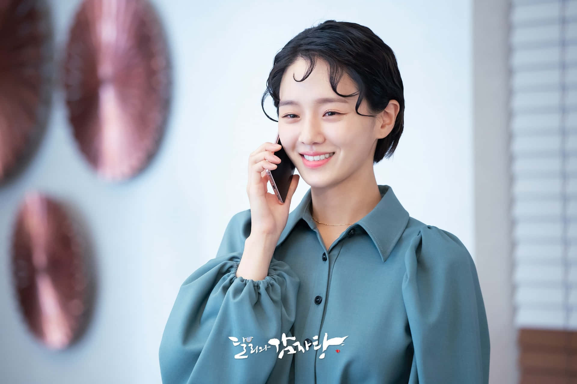 女子在現代室內環境中，對著圓形牆飾微笑講電話。