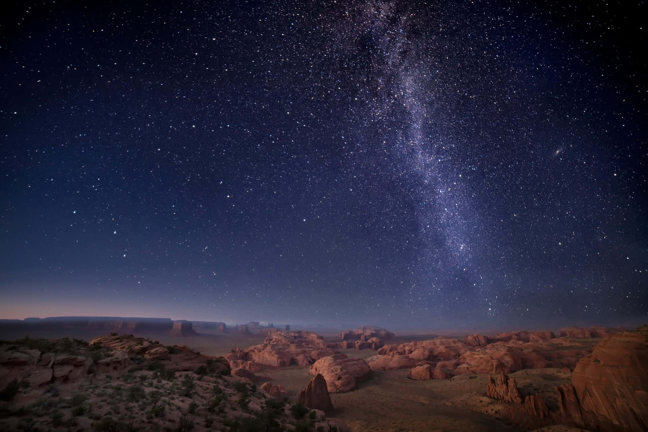 「仰望星空，讓星星閃耀」 壁紙 — 銀河系在夜晚燦爛地拱起於沙漠峽谷之上，下方是發光的紅色岩層。