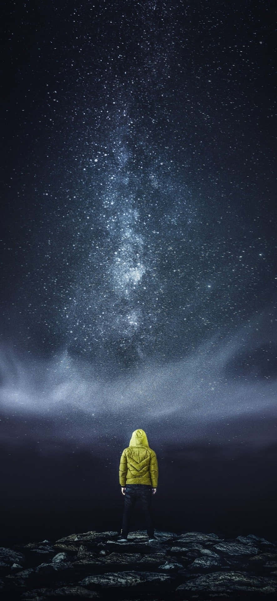 穿著黃色連帽衫的人站在岩石上，星空下銀河閃耀