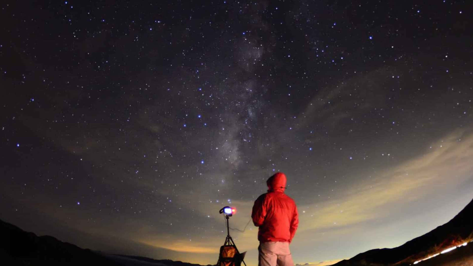 穿著紅色外套的人夜晚站在山上觀看星星和銀河。