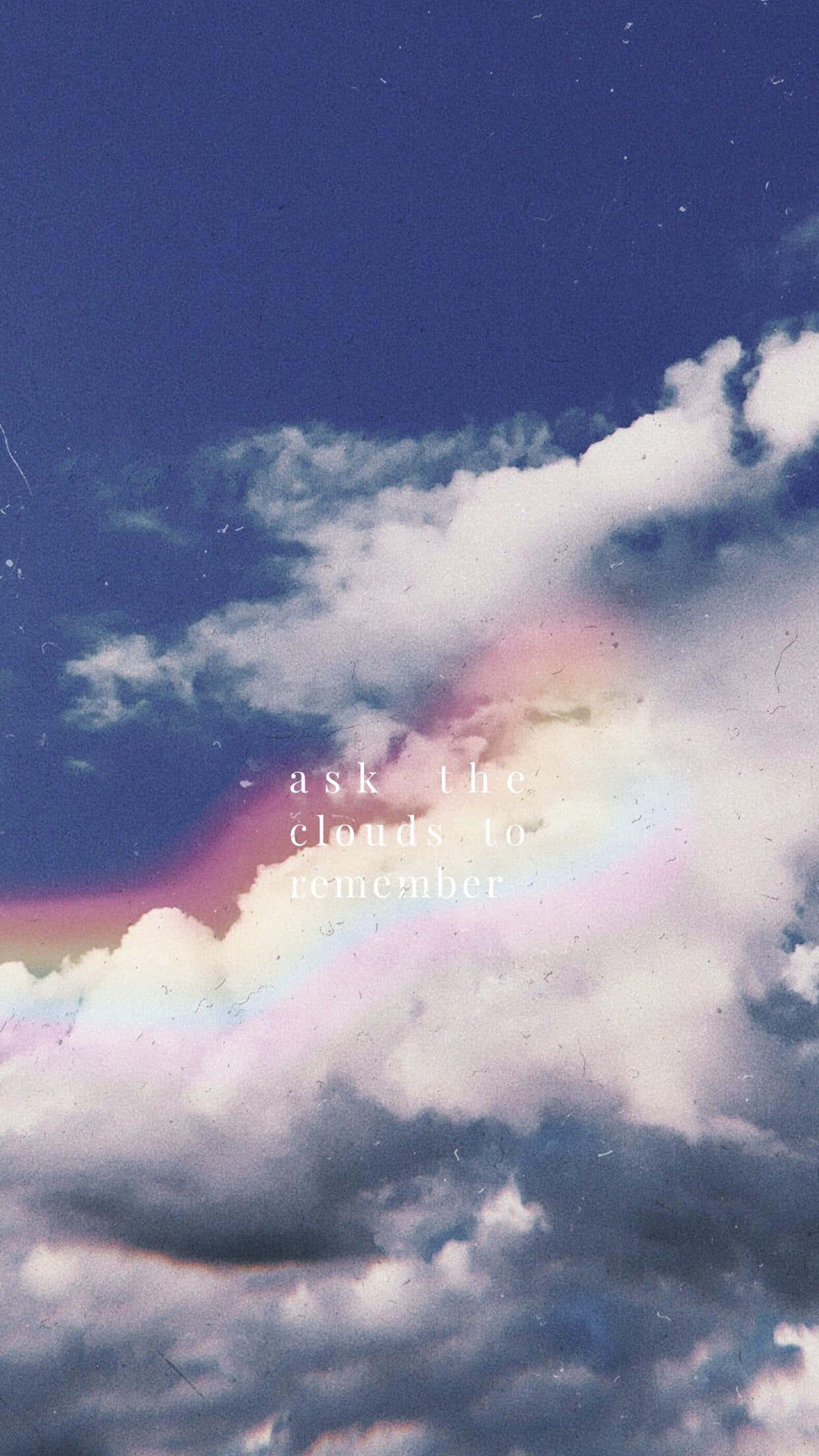 仰望藍天 壁紙 — 夢幻的天空，有柔軟的雲朵和一道微弱的彩虹，透過復古菲林顆粒閃耀。