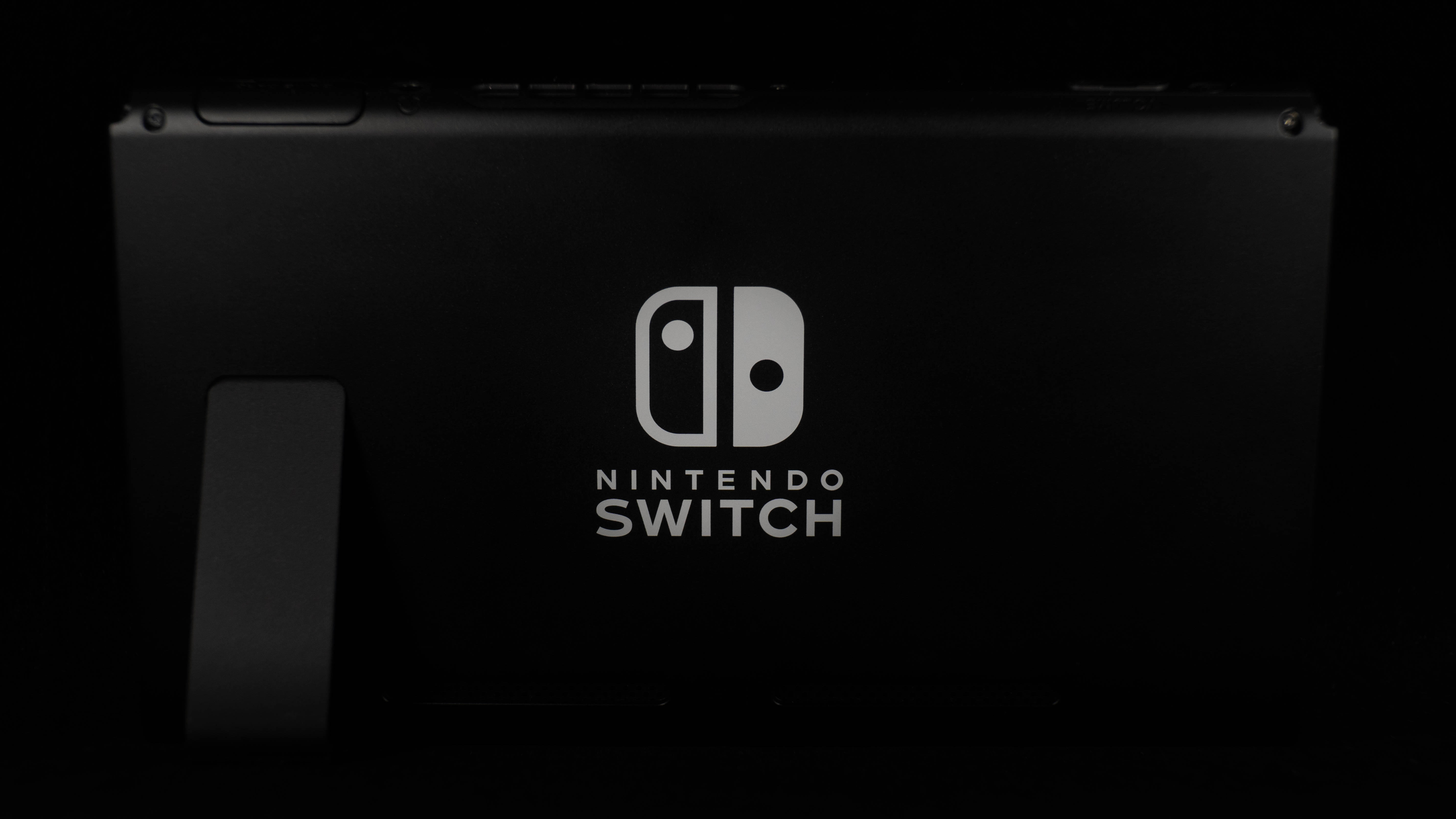 任天堂Switch搖桿 壁紙 — 光滑的黑色Nintendo Switch主機在漆黑背景上微微發光，突顯其簡約設計和標誌性標誌。