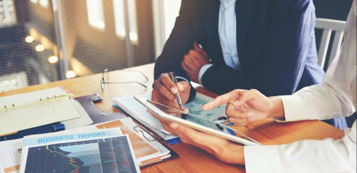 企業同仁討論業務 壁紙 — 兩位專業人士在現代辦公室環境中協作查看平板電腦上的財務圖表。