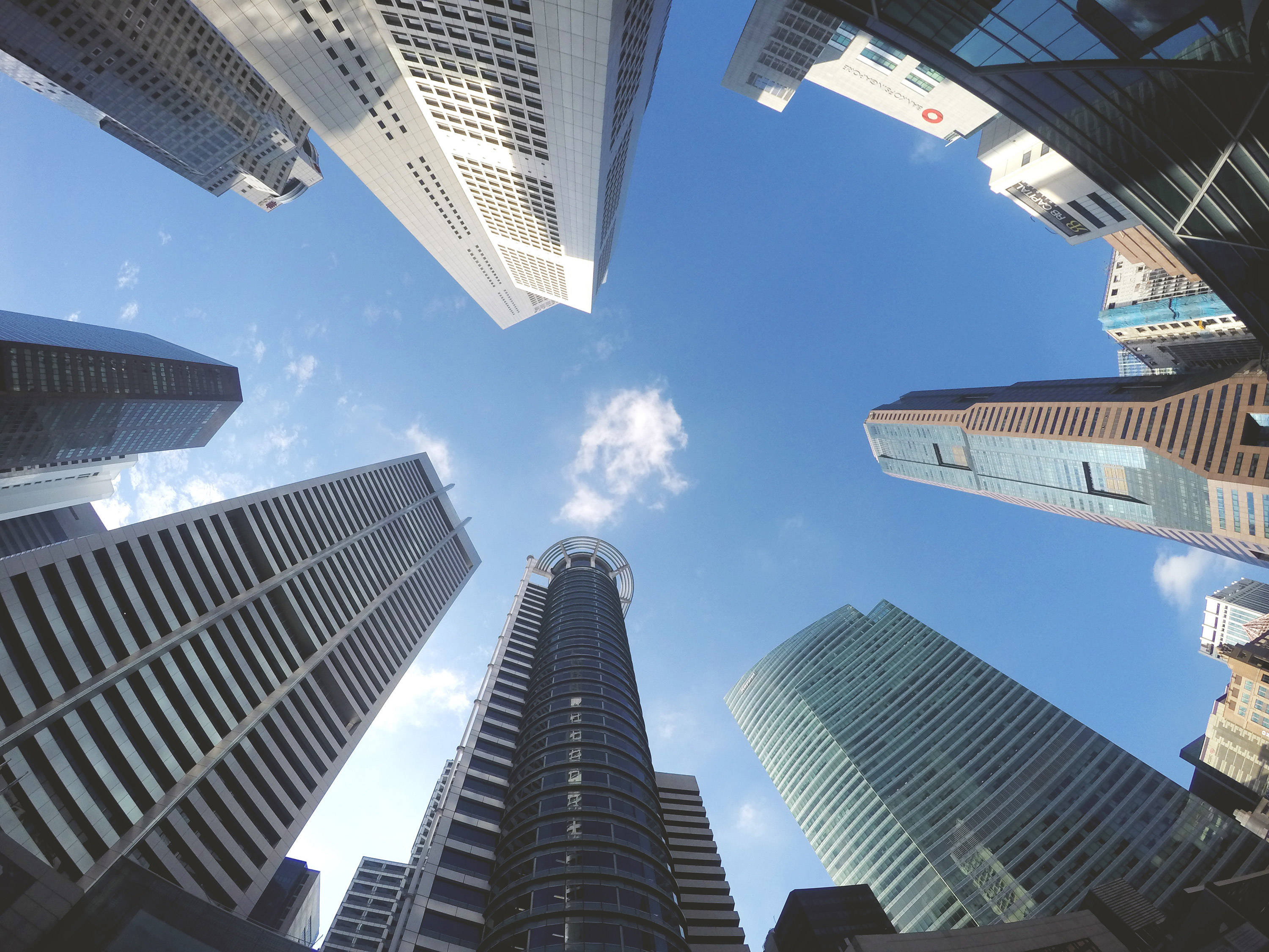 企業都市摩天大樓 壁紙 — 高聳的摩天大樓匯聚向明亮的藍天，天空中有散落的雲朵，呈現戲劇性的低角度城市拍攝。