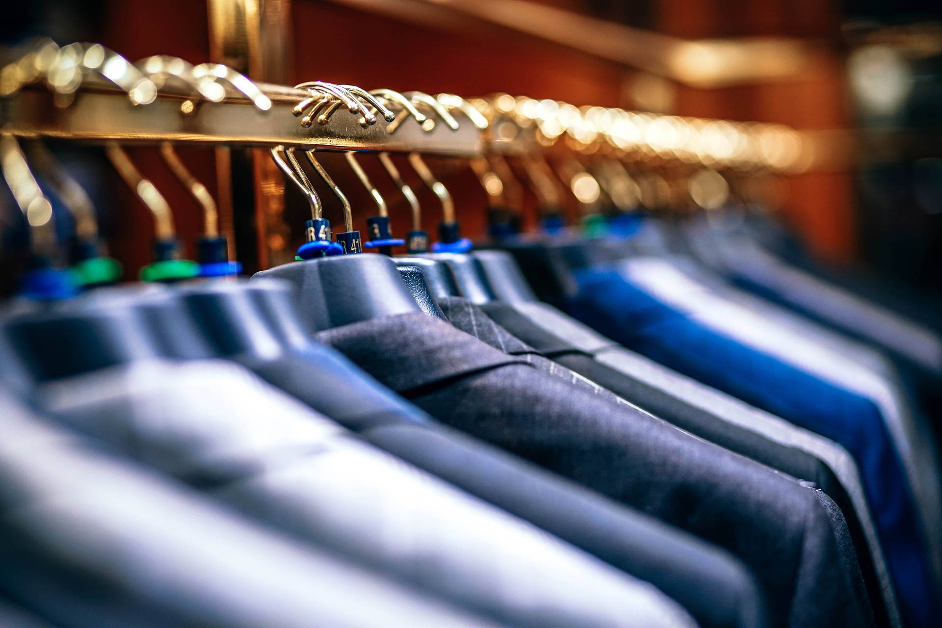 在燈光溫暖的精品店中，金色衣架上整齊排列的深色西裝。