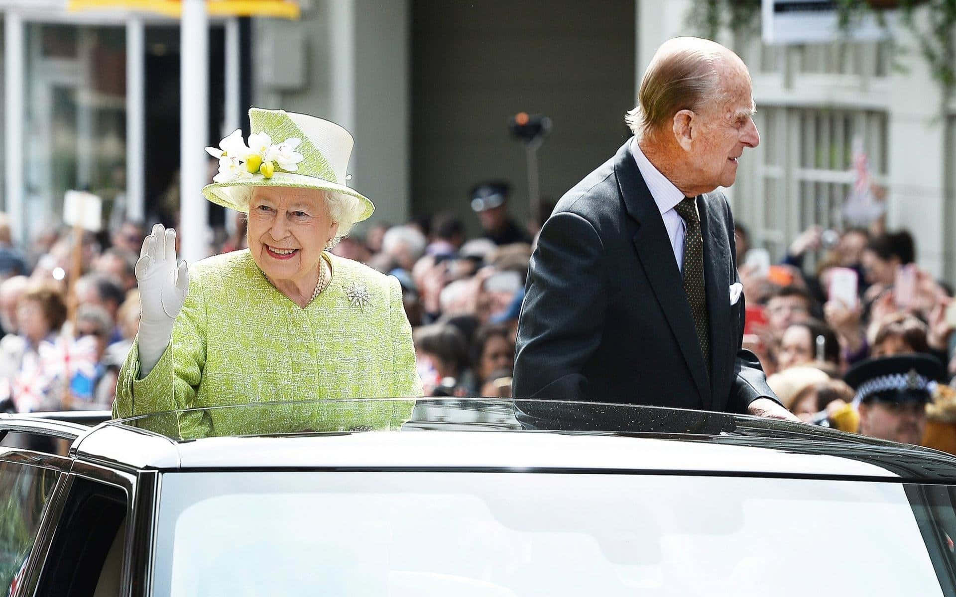 Queen Elizabeth 桌布 壁紙 — 伊利沙伯二世女王在公眾巡遊期間從車窗愉快地揮手，菲臘親王站在她身旁。