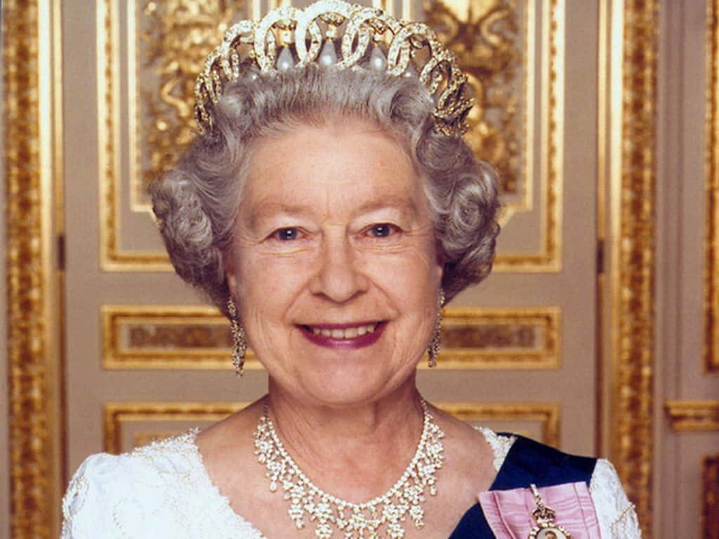 Queen Elizabeth 桌布 壁紙 — 伊利沙伯二世女王戴著鑲有寶石的王冠和珍珠項鍊，在金色華麗的門背景下溫暖地微笑。