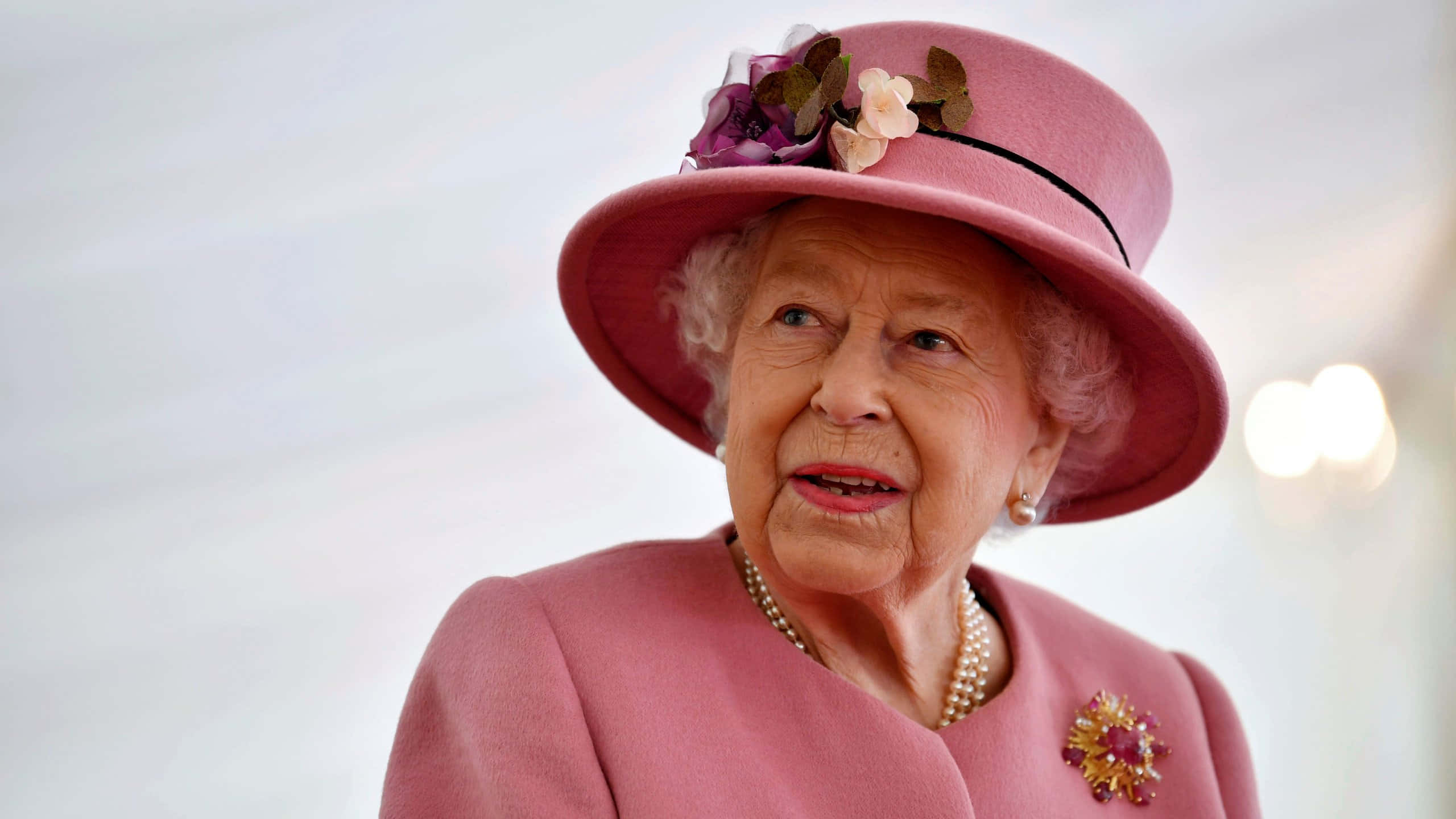 Queen Elizabeth 桌布 壁紙 — 伊利沙伯二世女王身穿粉紅色外套和飾有花朵的配套帽子，以溫柔的表情向上仰望。