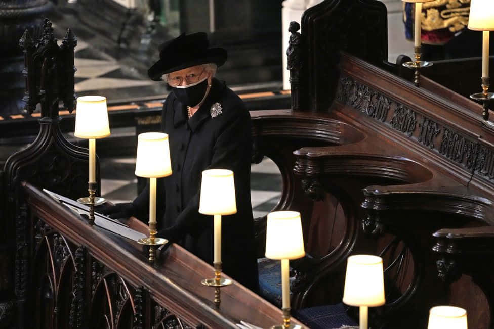 Funeral 桌布 壁紙 — 伊利沙伯二世女王身穿黑色外套和帽子，莊嚴地站在宏偉大教堂中由溫暖燭光照亮的華麗木製長椅後面。