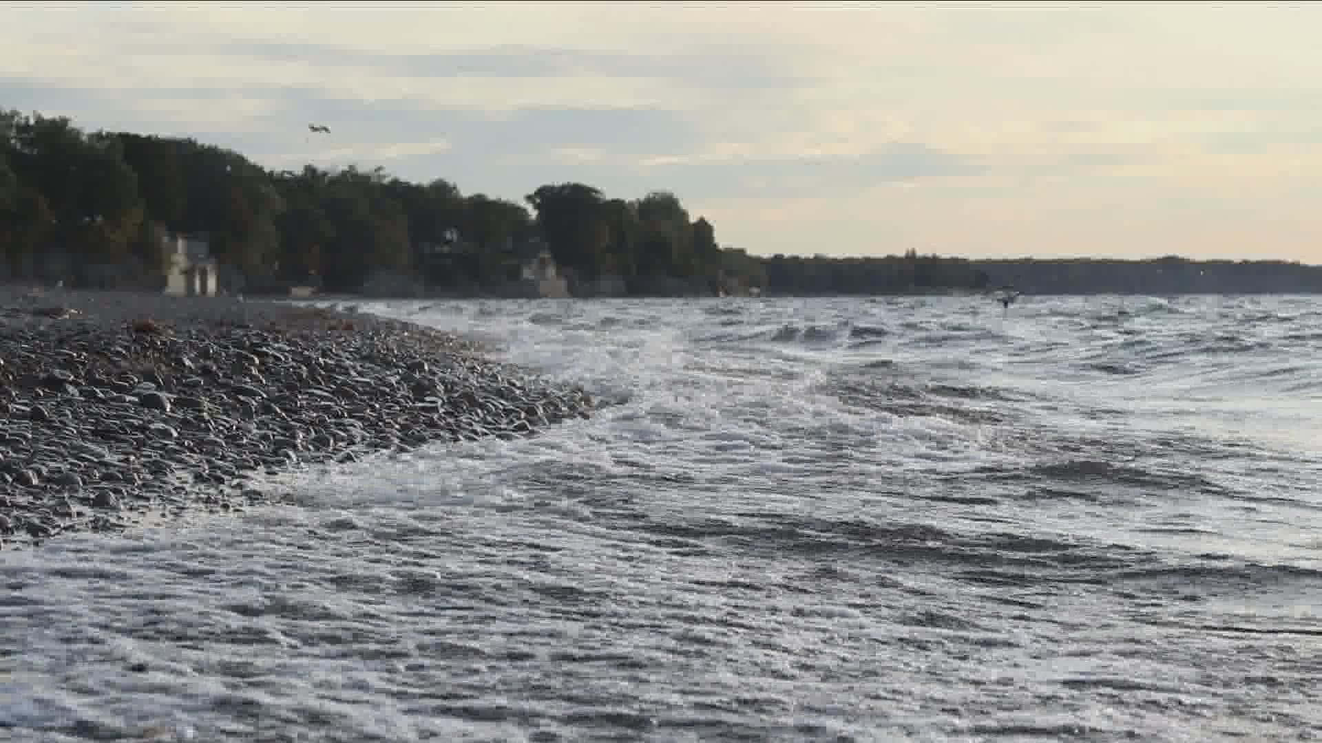 黃昏時分，海浪拍打岩石海灘，遠處有樹木和房屋。
