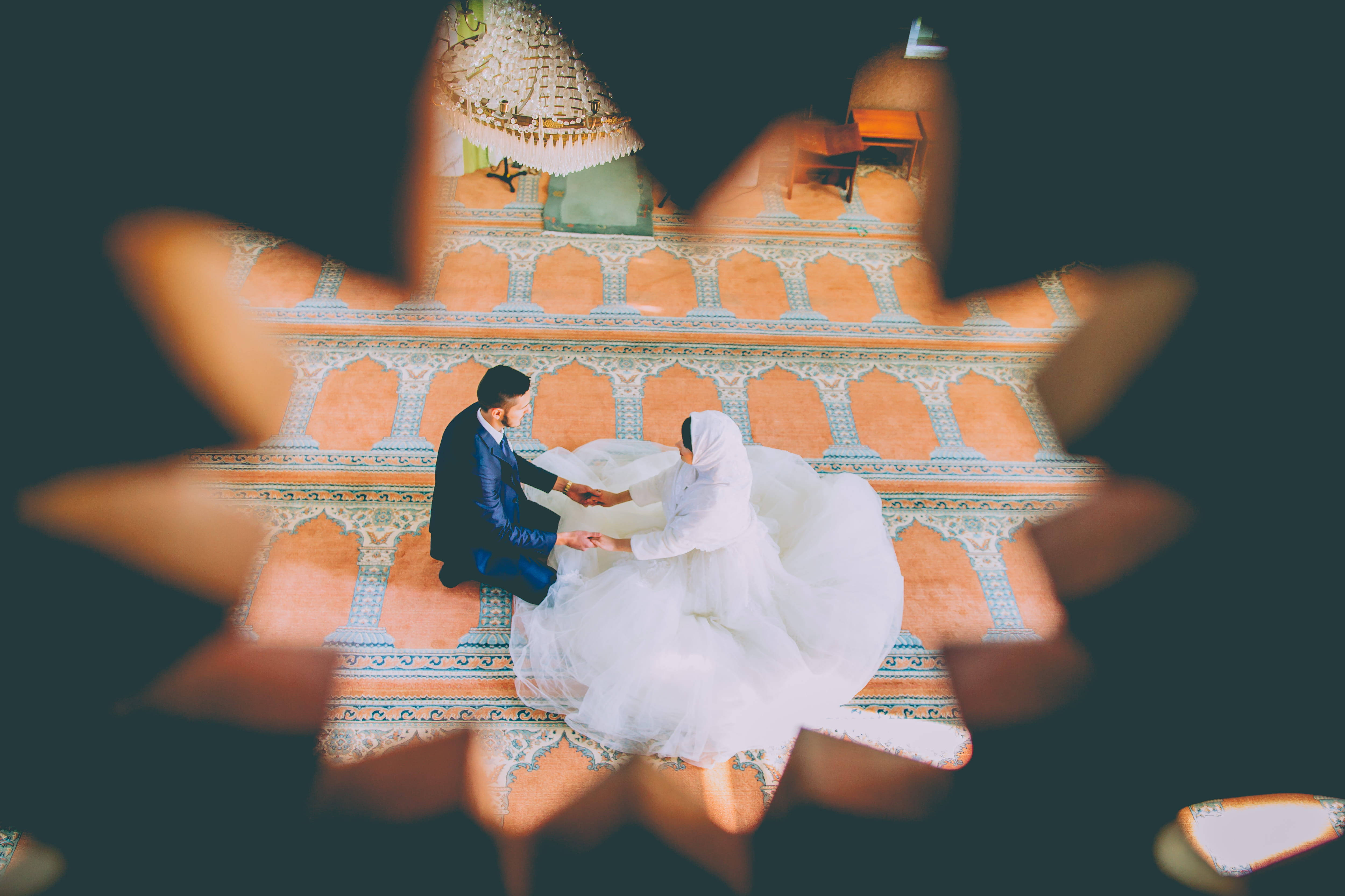 伊斯蘭婚紗 壁紙 — 一對夫婦在圖案清真寺地板上跪著祈禱，透過星形鏡頭光暈觀看。