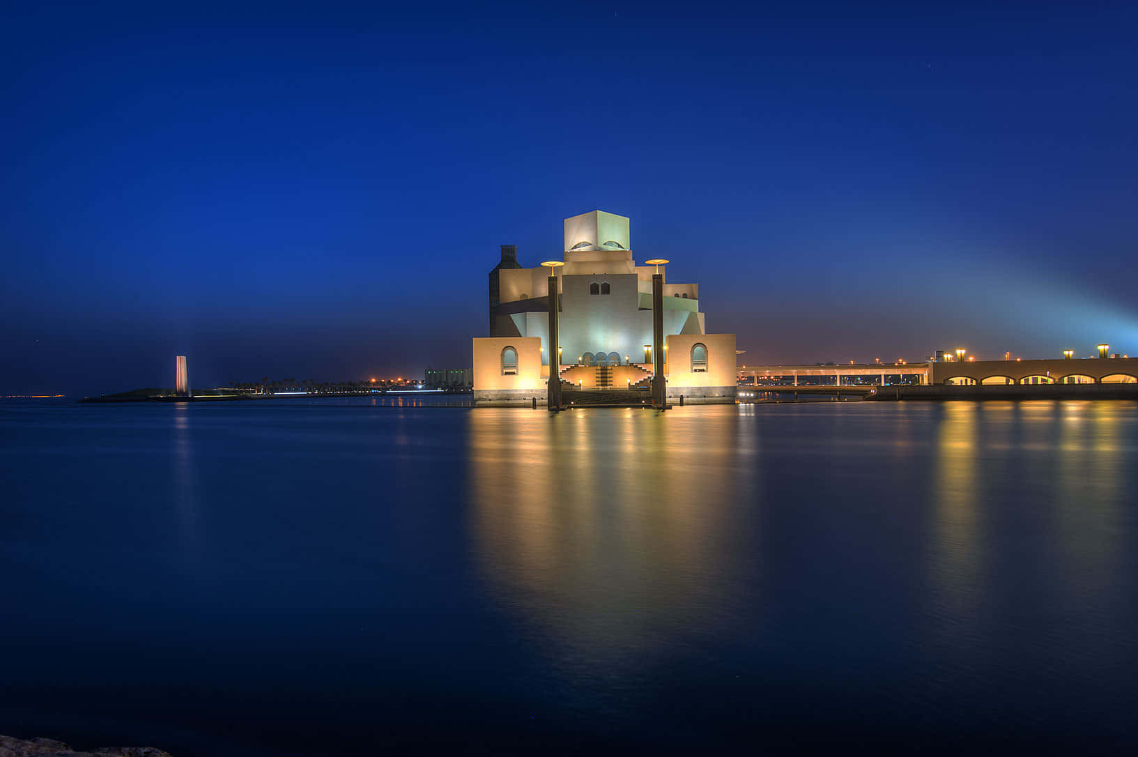 伊斯蘭藝術博物館夜間倒映於海面 壁紙 — 一座現代博物館在夜晚亮燈，在深藍色天空下平靜的水面上美麗地倒映。