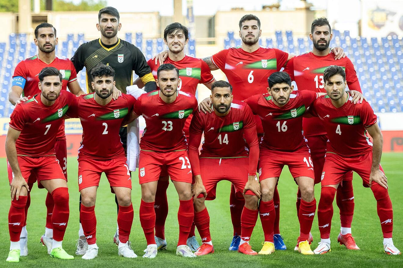 Iran 桌布 壁紙 — 伊朗國家足球隊身穿紅色球衣，在綠色球場上自信地擺姿勢，身後是體育場座位。