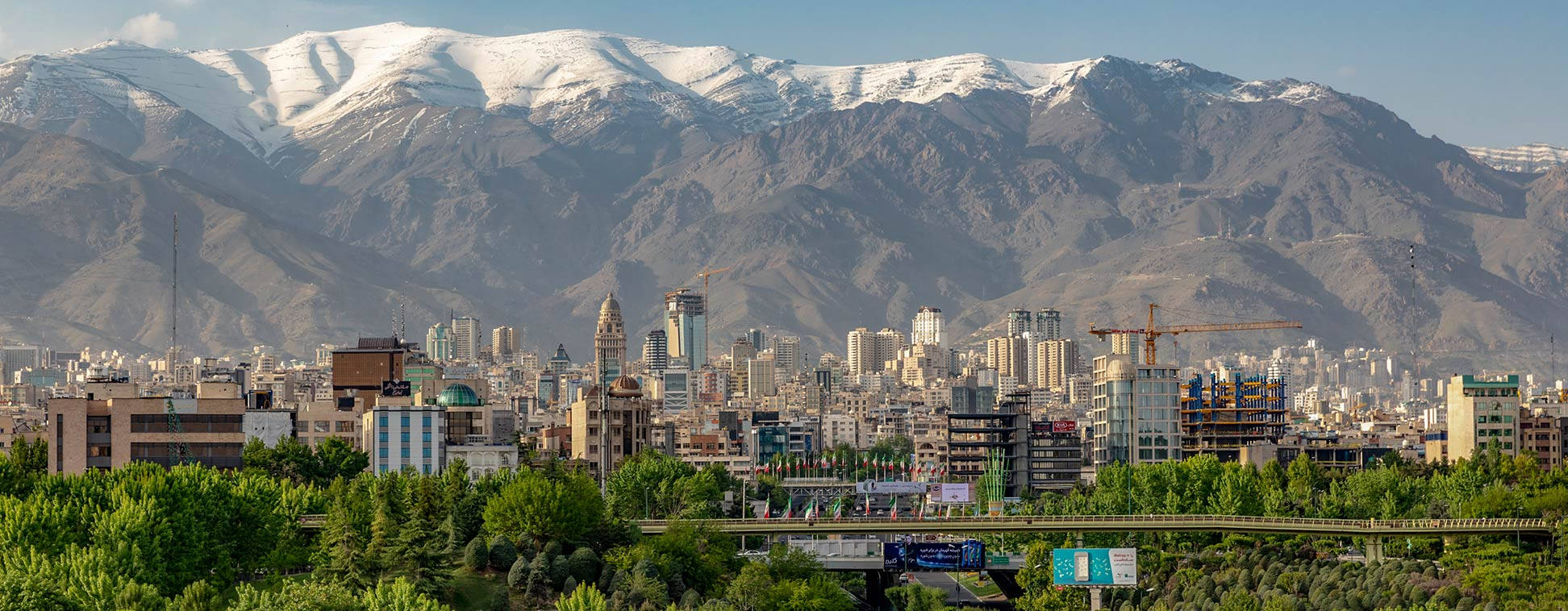 伊朗城市的壯麗景色 壁紙 — 在晴朗藍天下，坐落於高聳雪山腳下的廣闊城市景觀。