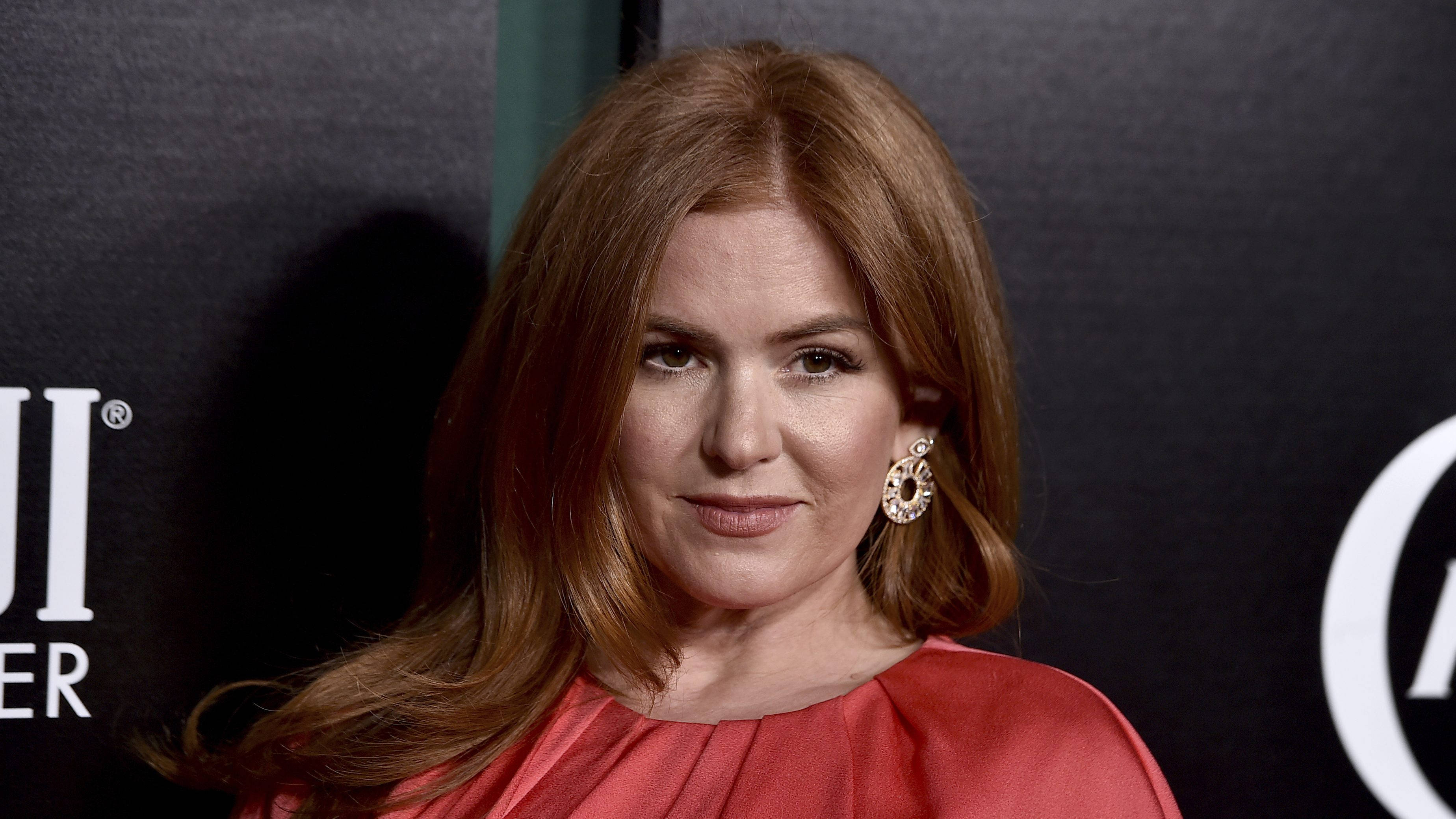 伊莎·費雪出席《TIME Women of the Year》 壁紙 — 一位紅髮紅裙的女性在深色品牌背景前對著鏡頭微笑。